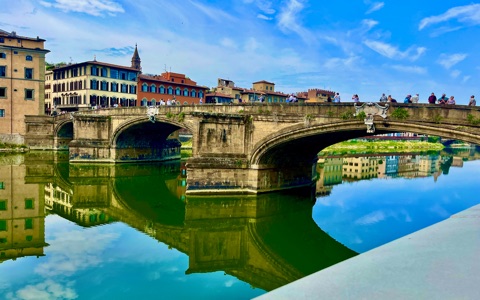 Florence riverside buildings reflected in the Arno beneath a blue sky