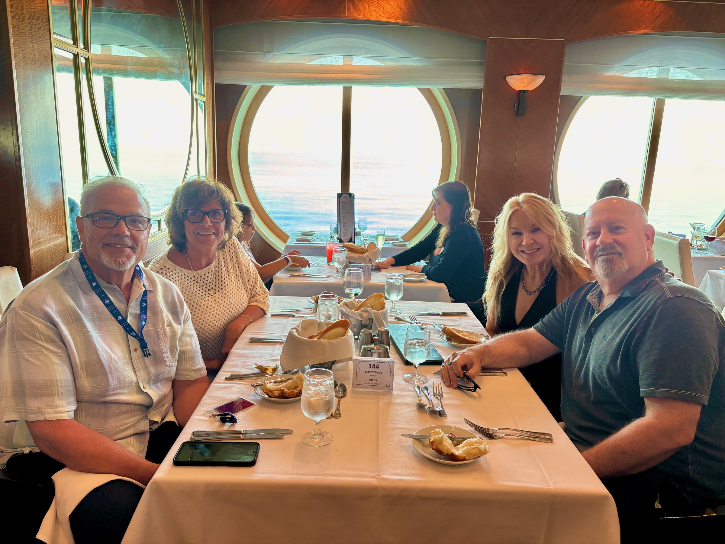 Steve and Dianne sharing dinner with friends beside large windows overlooking the sea