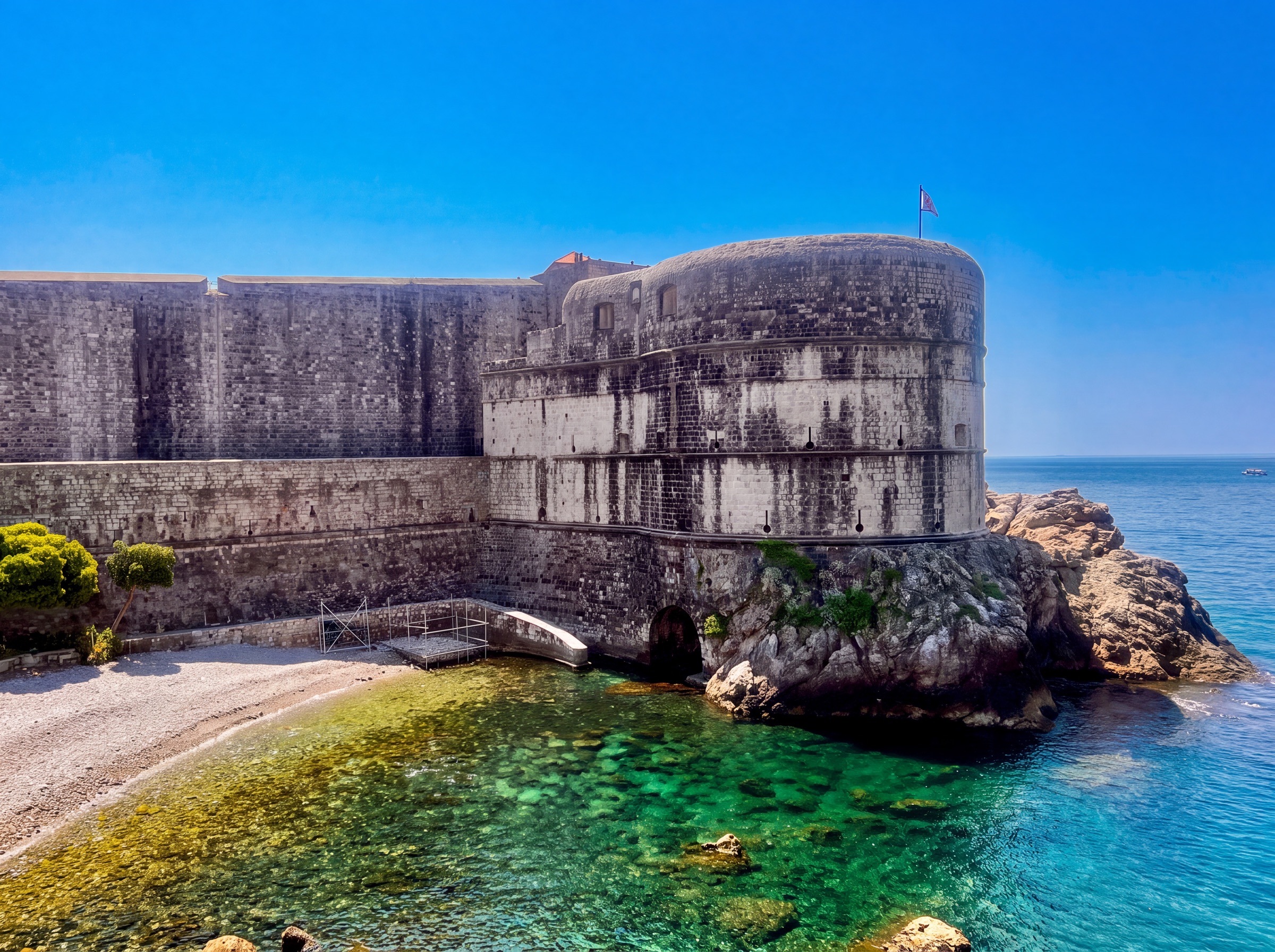 Round stone tower and city walls meeting the clear Adriatic coastline