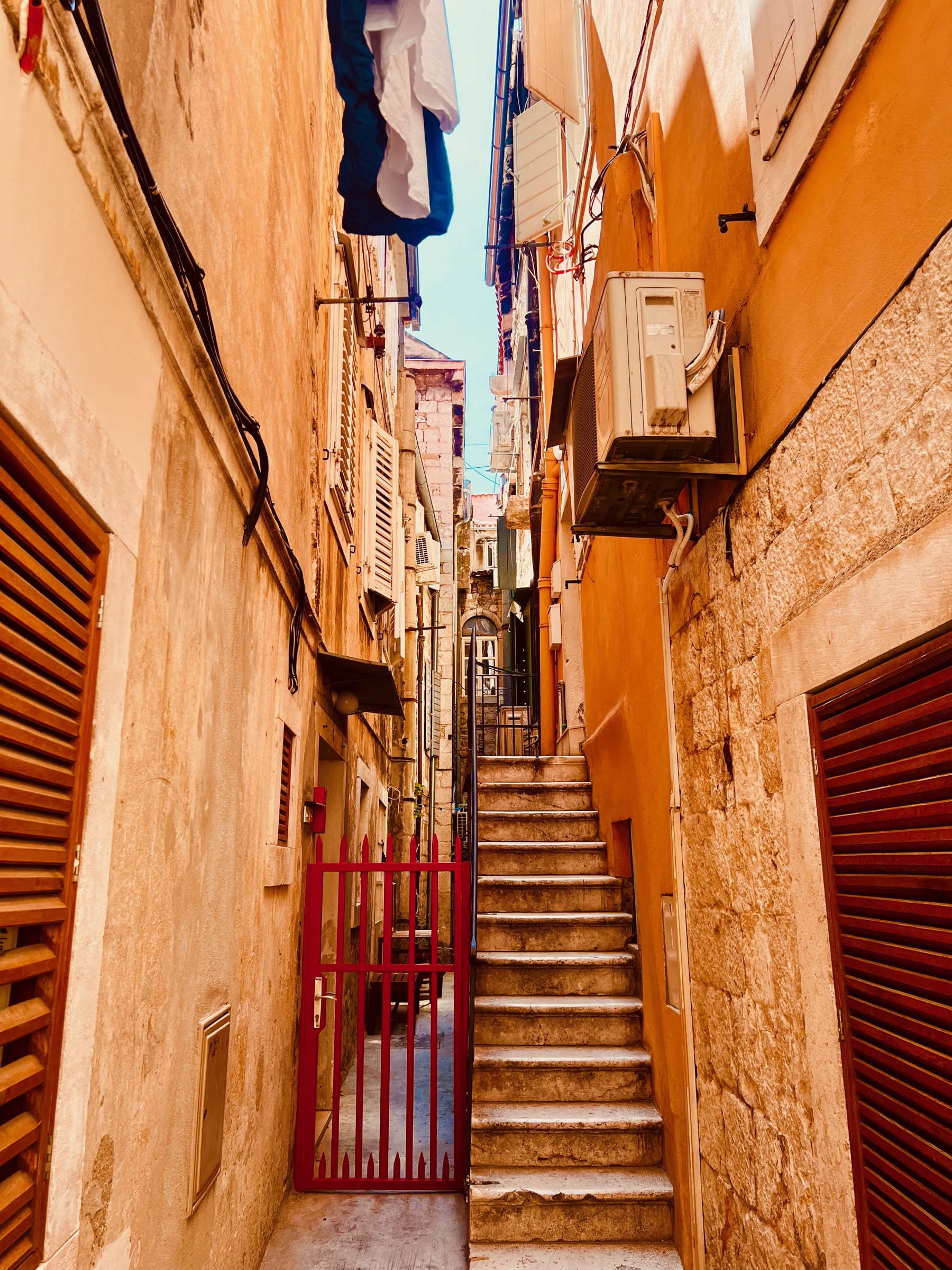 A narrow residential alley in Split with warm walls, stone steps, and a red gate