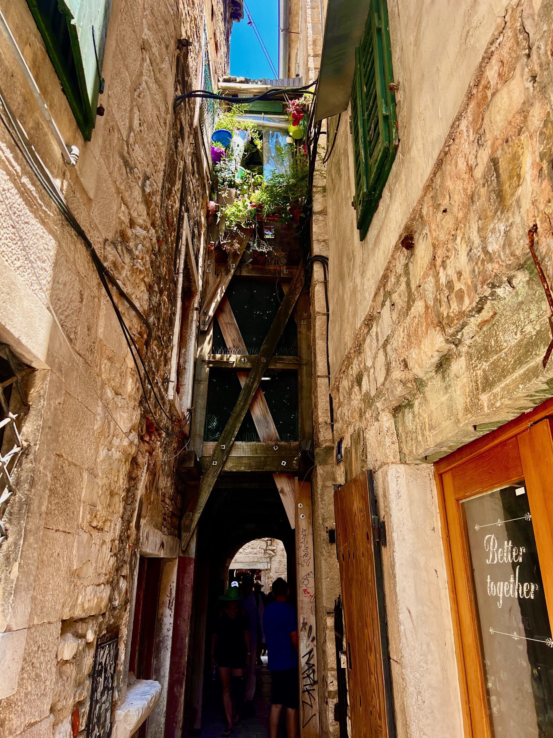A narrow stone passage with plants and homes above an archway in Split