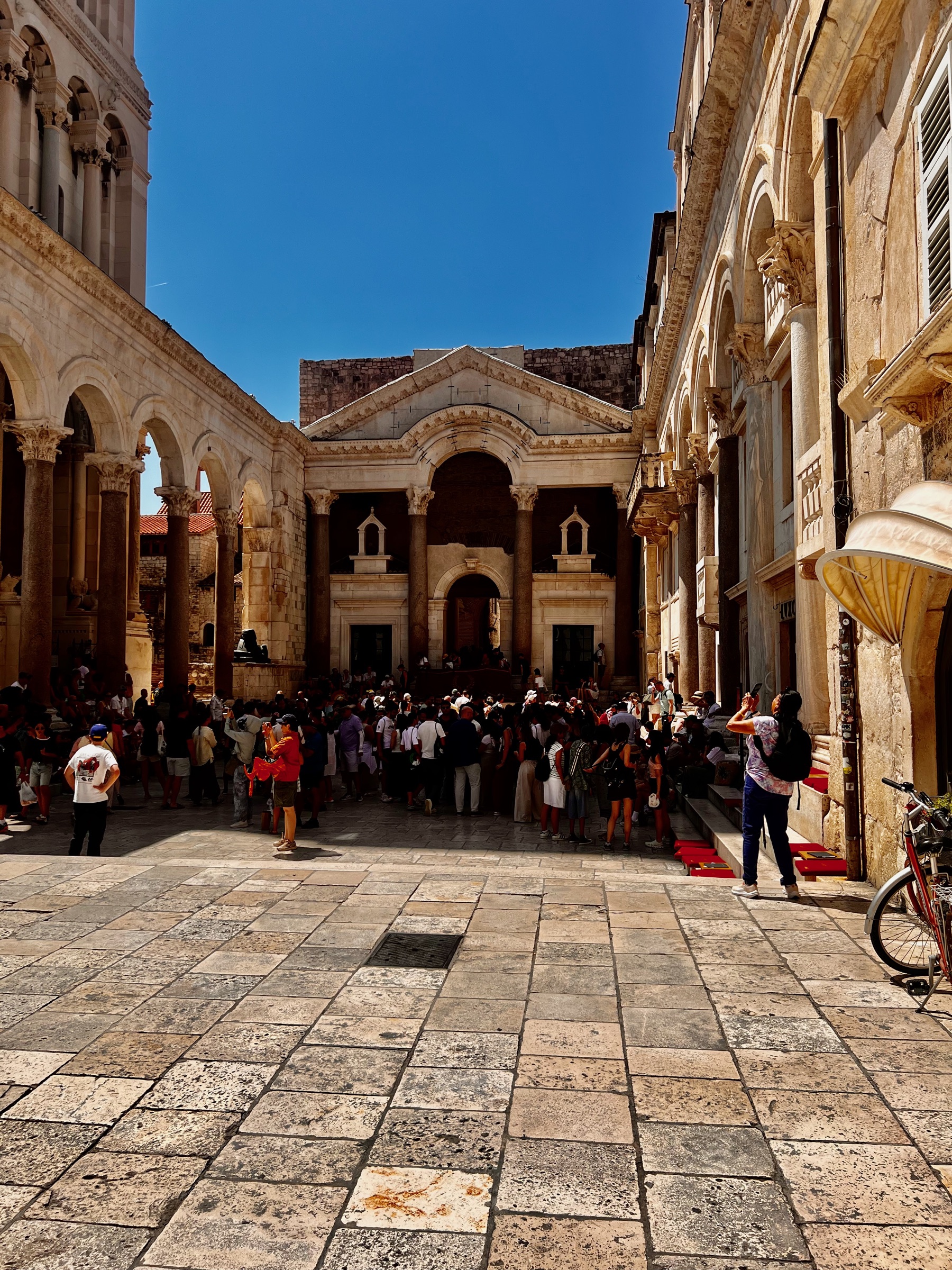 The columned Peristyle of Diocletian's Palace filled with visitors beneath a blue sky