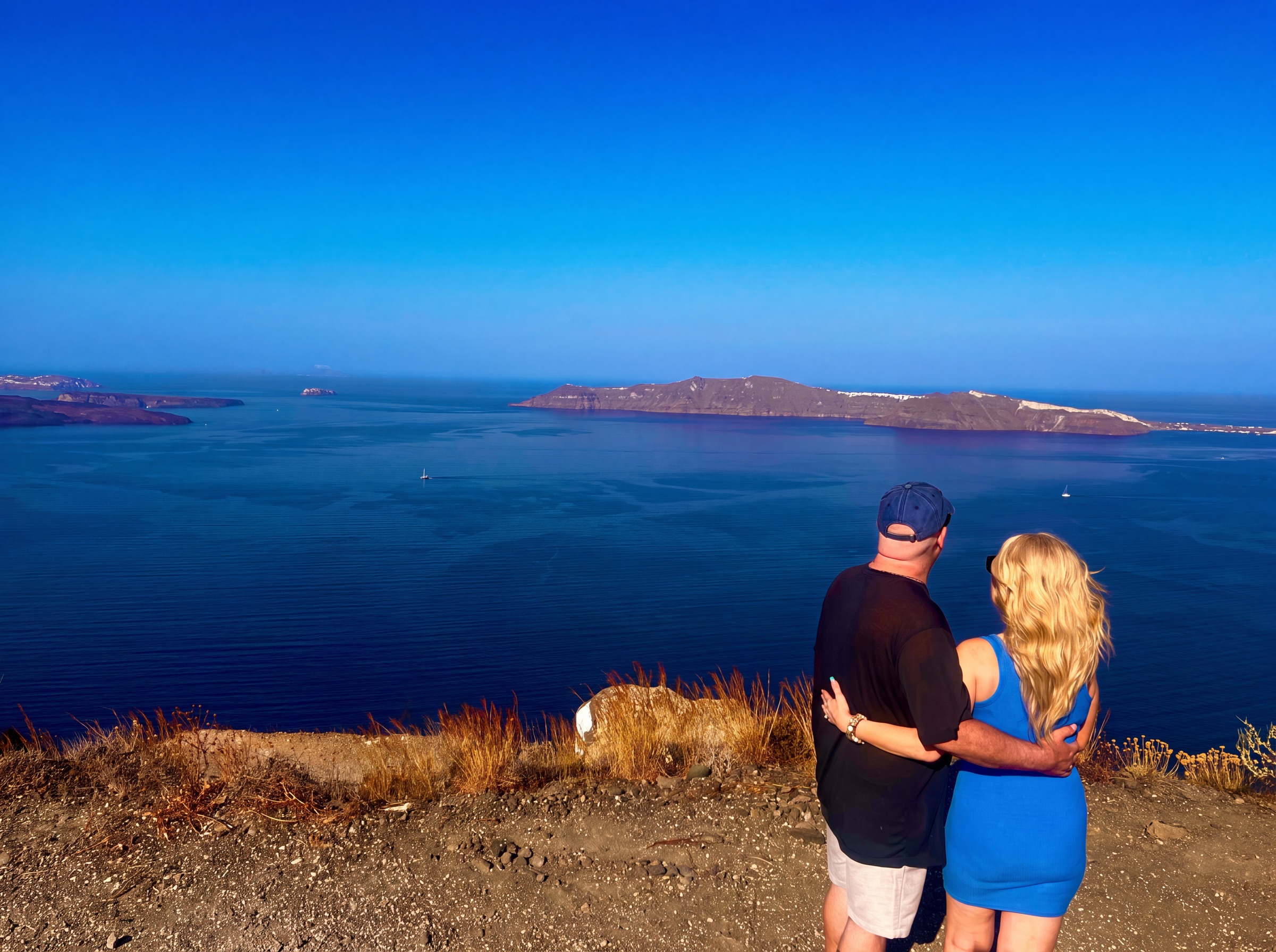 Dianne and Steve embracing while looking across Santorini's blue caldera