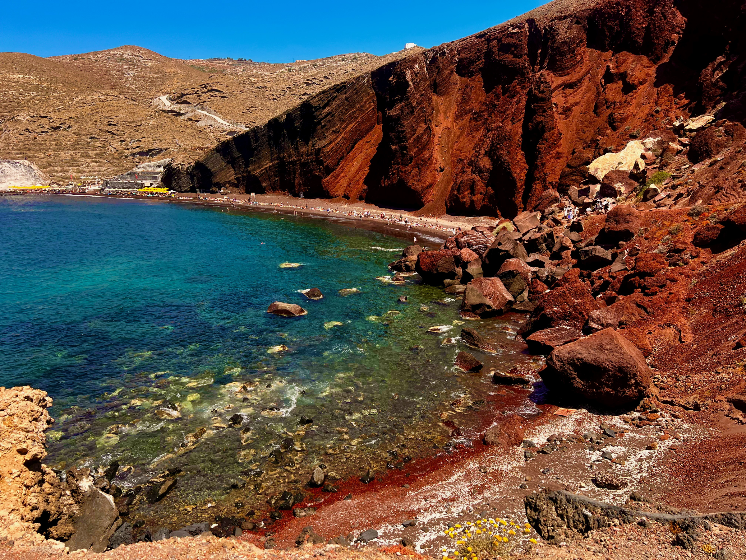 Red volcanic cliffs curving around clear turquoise water at Santorini's Red Beach