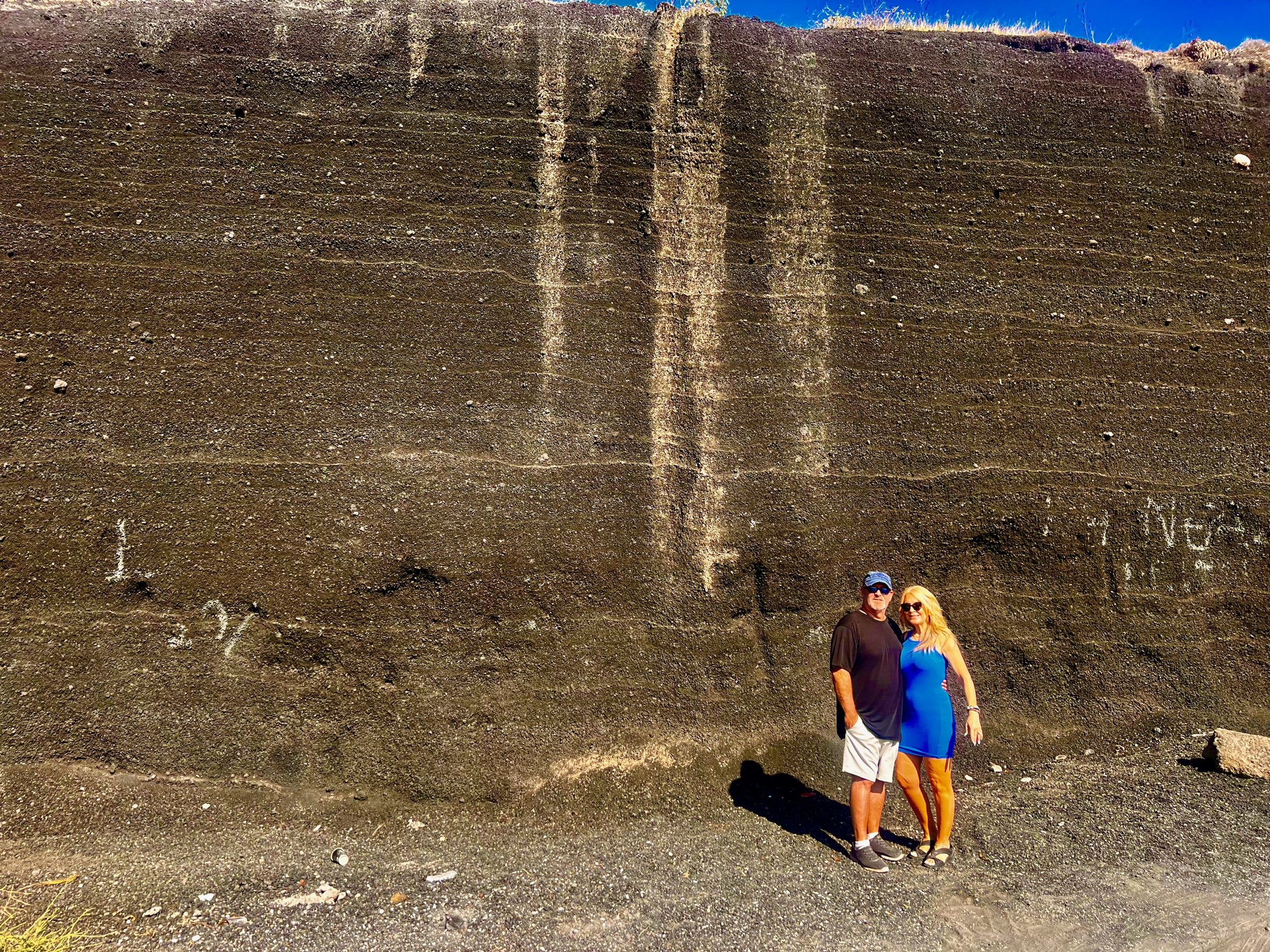 Dianne and Steve standing beneath a towering wall of dark volcanic ash