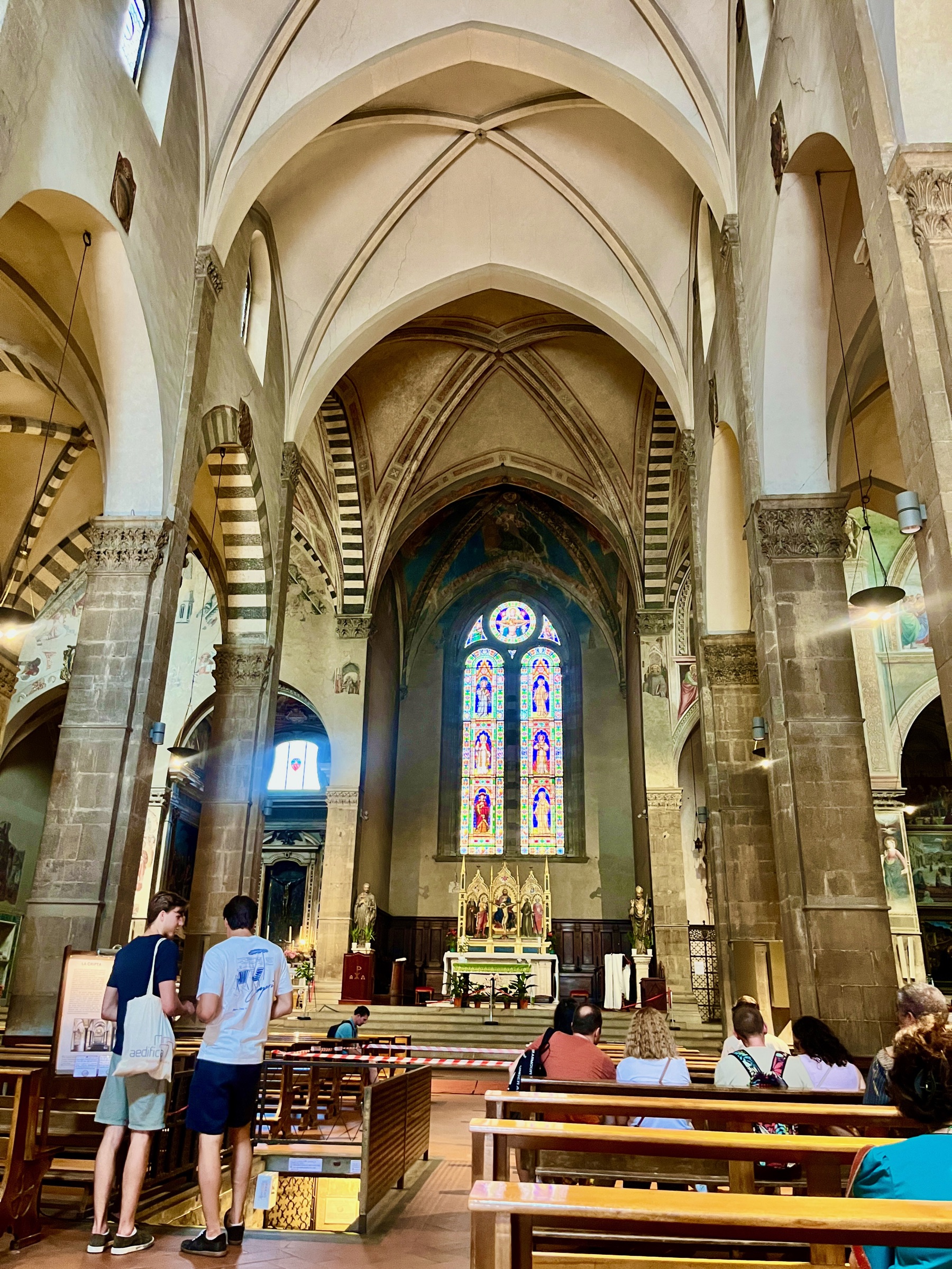 Florentine church interior with high vaulted arches and a glowing stained-glass window