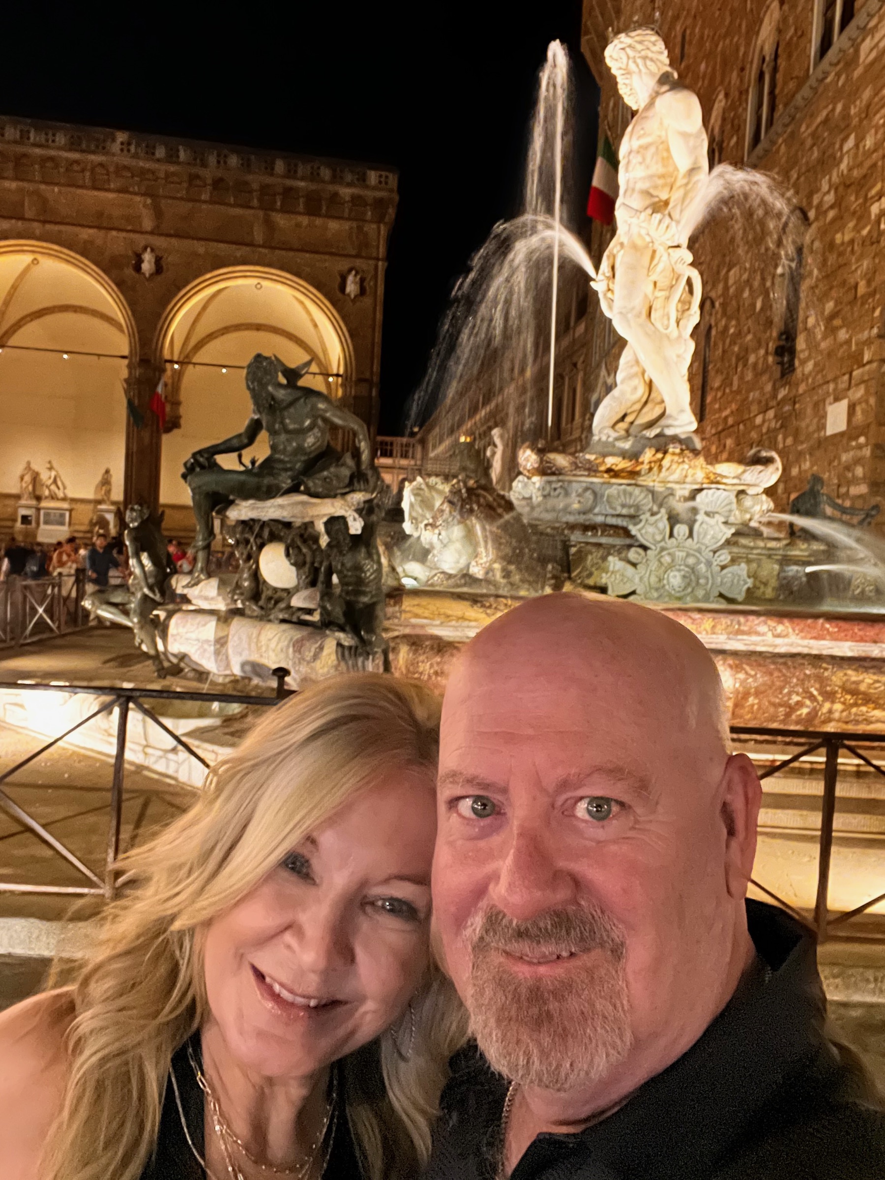 Dianne and Steve smiling together beside the illuminated Neptune fountain