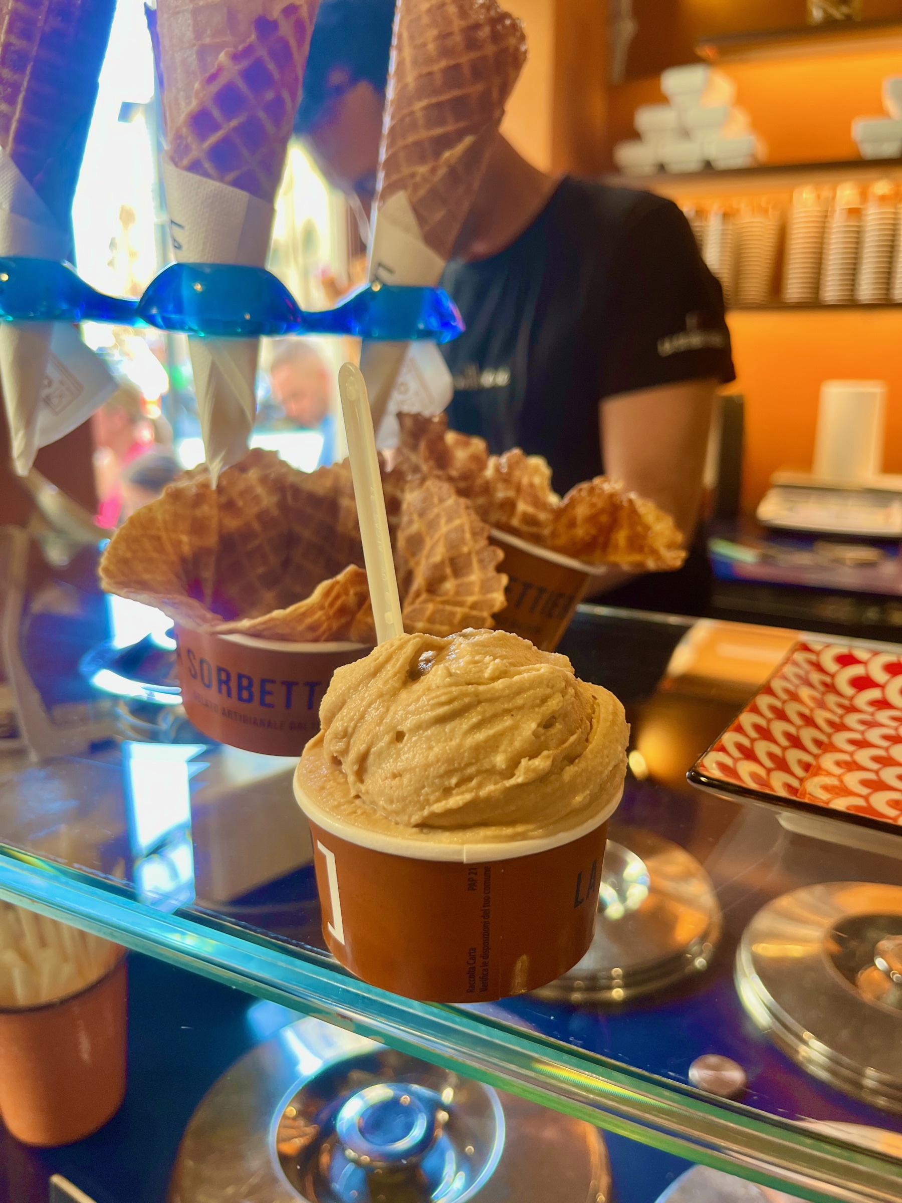 A cup of Italian gelato displayed beside stacked waffle cones