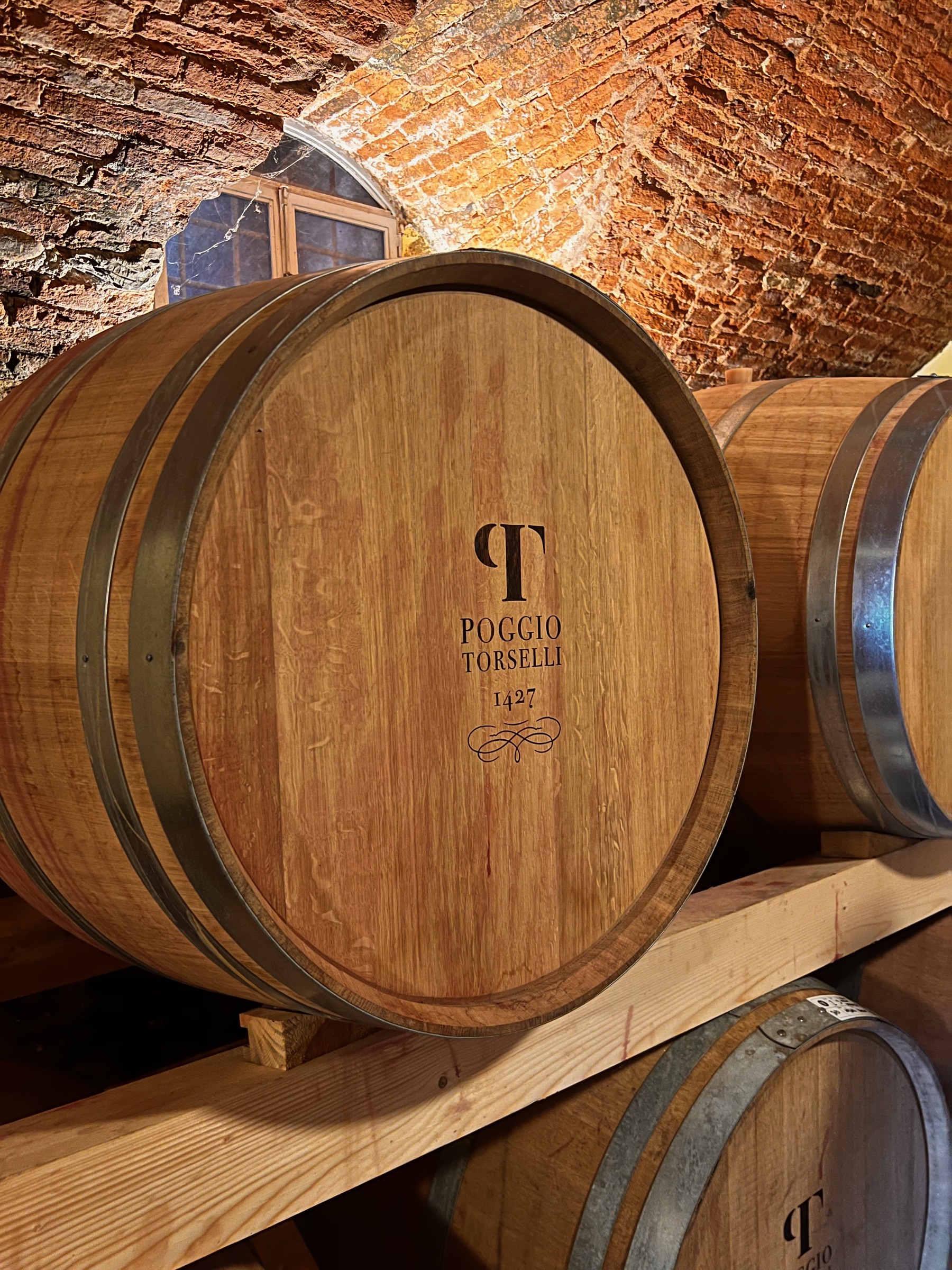 Large wooden wine barrels resting beneath the brick-vaulted ceiling of a Tuscan cellar