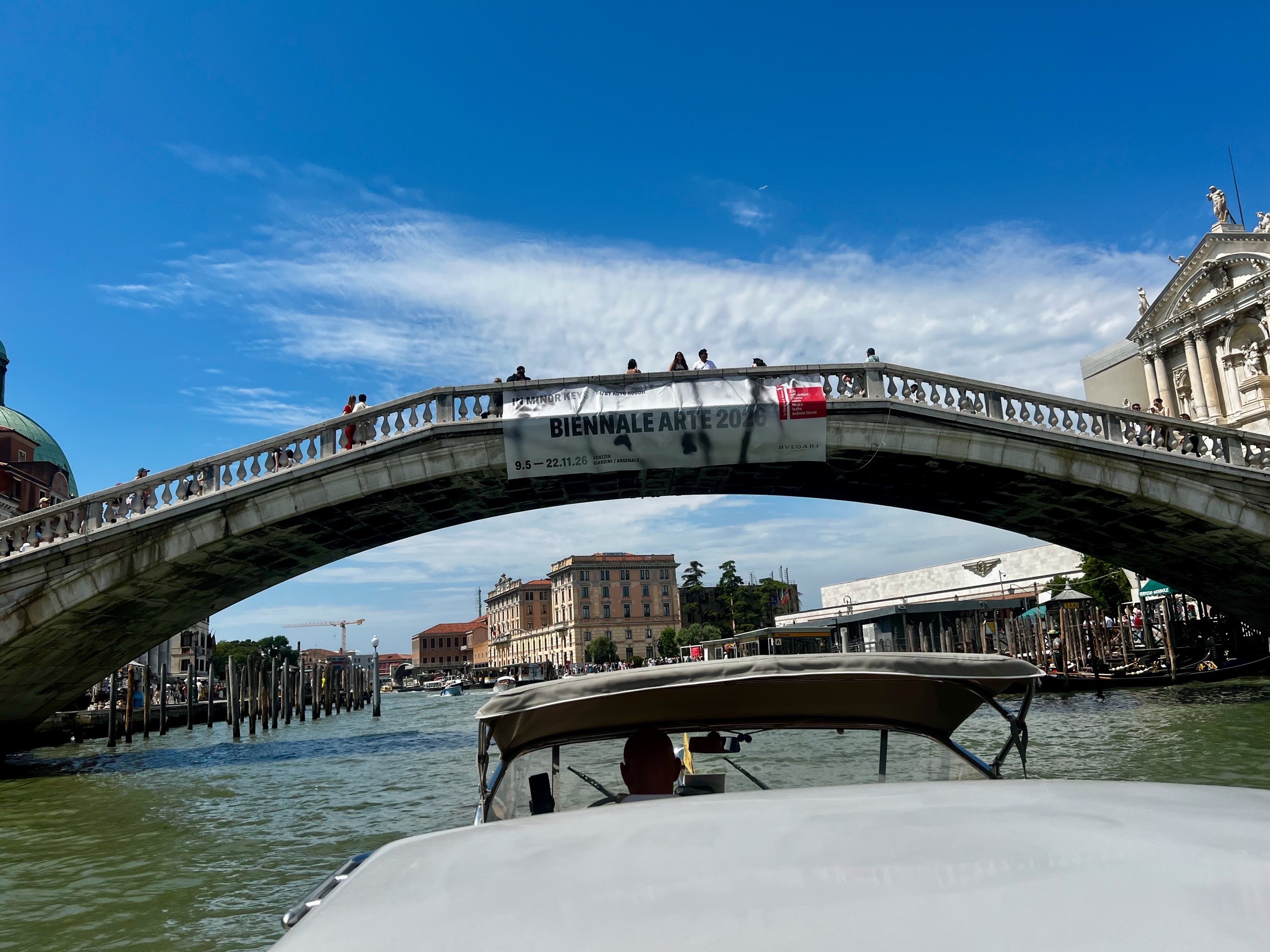 View from a water taxi approaching an arched bridge crowded with pedestrians in Venice